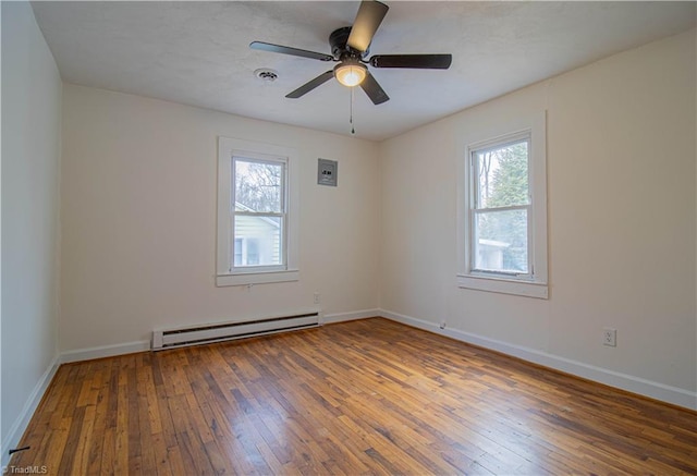 empty room featuring a baseboard heating unit, wood-type flooring, baseboards, and a healthy amount of sunlight