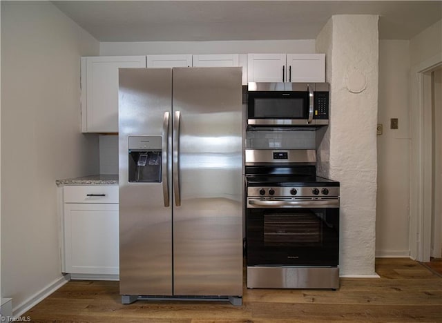 kitchen featuring stainless steel appliances, wood finished floors, white cabinets, light stone countertops, and baseboards