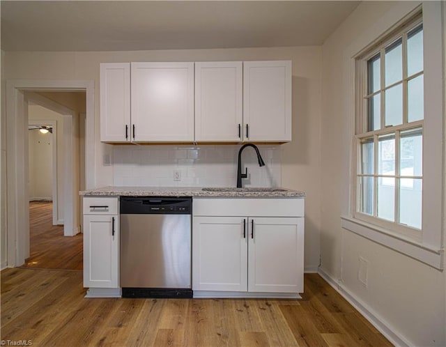 kitchen with stainless steel dishwasher, light wood-type flooring, a sink, and white cabinets