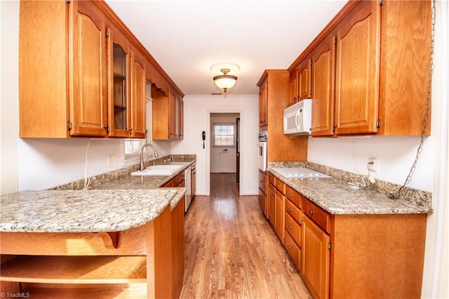 kitchen with sink, light stone counters, kitchen peninsula, white appliances, and light hardwood / wood-style floors