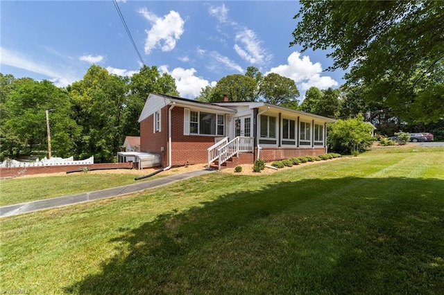 view of front facade with a sunroom, brick siding, and a front yard