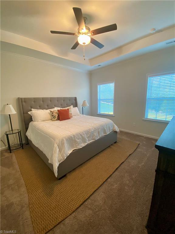 bedroom with ceiling fan, a tray ceiling, and dark colored carpet