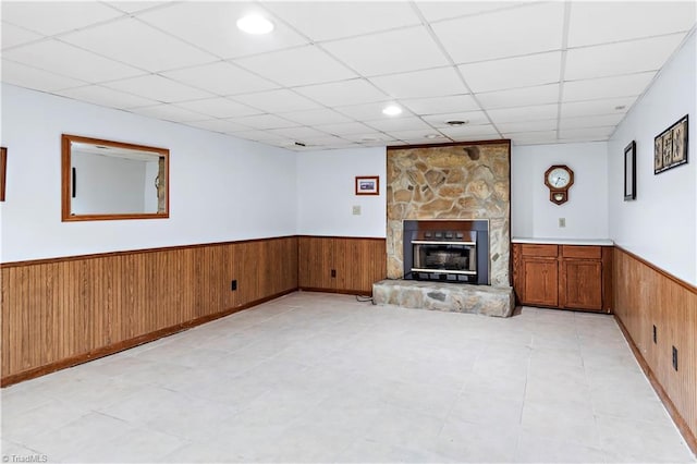 unfurnished living room with light tile patterned flooring, a drop ceiling, wooden walls, a wainscoted wall, and a fireplace