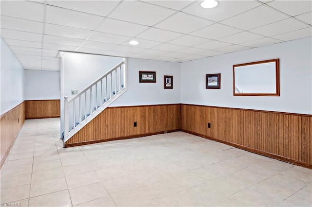 basement with stairway, wooden walls, a wainscoted wall, and a drop ceiling