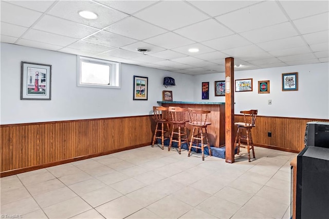 bar featuring wood walls, a wainscoted wall, a drop ceiling, and a bar
