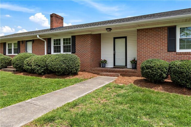 view of front of house featuring brick siding, a chimney, and a front yard