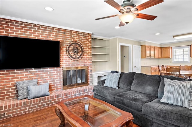 living area featuring recessed lighting, a brick fireplace, wood finished floors, ceiling fan, and ornamental molding