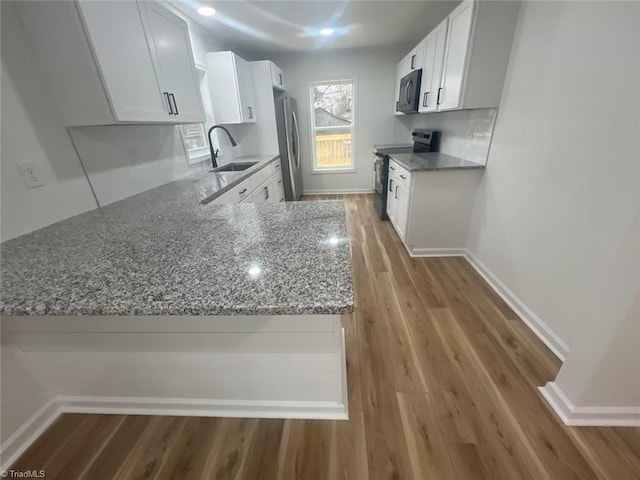 kitchen with black appliances, white cabinets, kitchen peninsula, and sink