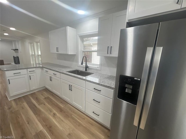 kitchen with white cabinets, sink, stainless steel refrigerator with ice dispenser, light stone countertops, and kitchen peninsula