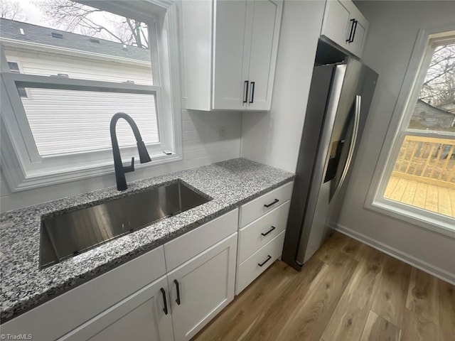 kitchen with white cabinets, stainless steel refrigerator, light stone countertops, and sink