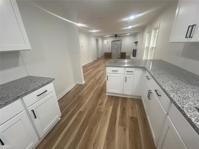 kitchen featuring kitchen peninsula, ceiling fan, dark hardwood / wood-style floors, light stone countertops, and white cabinetry