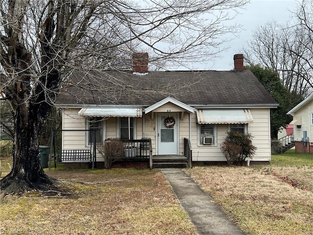 bungalow-style house featuring a shingled roof, a front yard, and a chimney