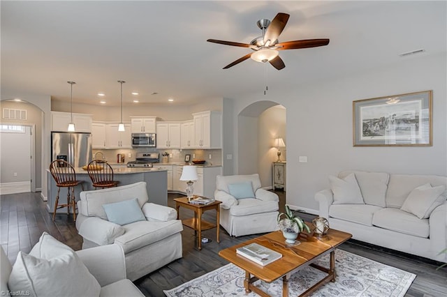 living area featuring baseboards, visible vents, arched walkways, and dark wood-type flooring