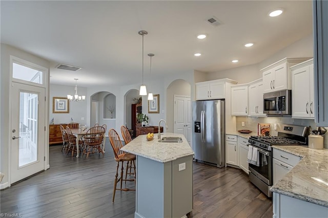 kitchen featuring a breakfast bar, dark wood finished floors, stainless steel appliances, visible vents, and a sink