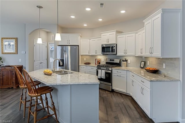 kitchen with dark wood finished floors, stainless steel appliances, tasteful backsplash, white cabinets, and a sink