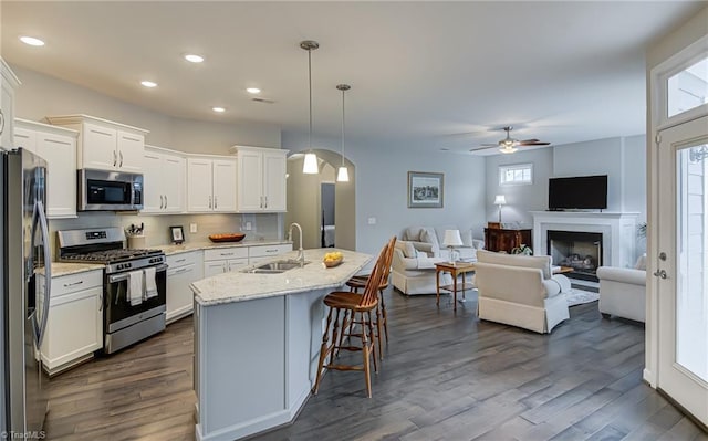 kitchen with stainless steel appliances, open floor plan, white cabinetry, a sink, and a kitchen breakfast bar