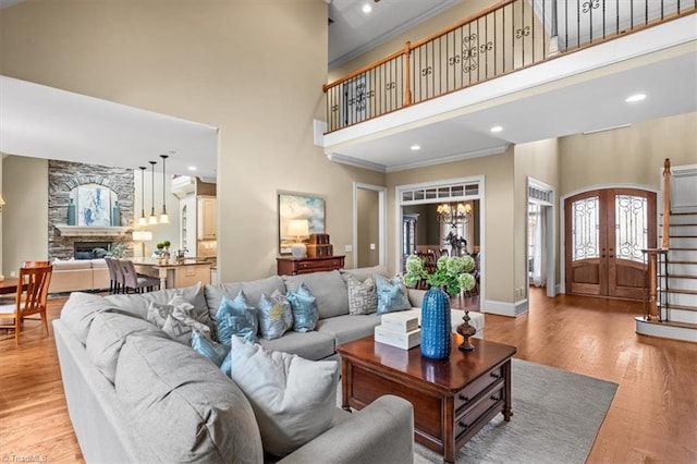 living area with arched walkways, a stone fireplace, crown molding, light wood finished floors, and a towering ceiling