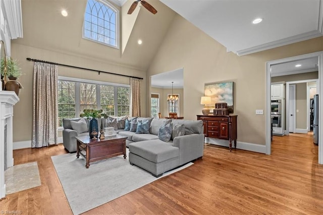 living room with light wood-type flooring, high vaulted ceiling, ceiling fan with notable chandelier, recessed lighting, and baseboards