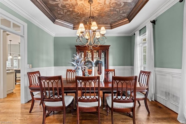 dining room featuring light wood finished floors, a notable chandelier, a raised ceiling, and a wainscoted wall