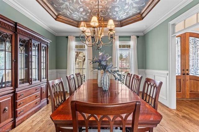 dining area featuring a chandelier, wainscoting, light wood finished floors, and a raised ceiling