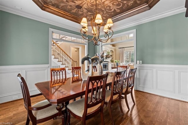 dining space featuring a raised ceiling, wood finished floors, a wainscoted wall, and a chandelier