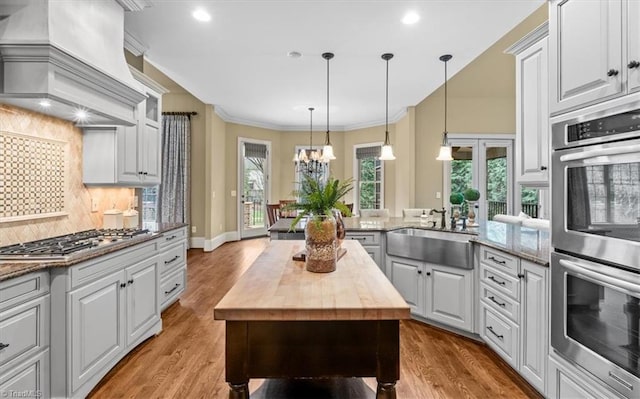 kitchen with wooden counters, ornamental molding, appliances with stainless steel finishes, custom exhaust hood, and a sink