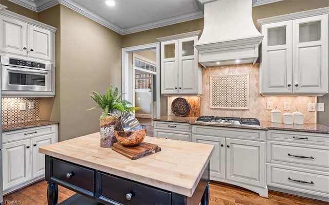 kitchen featuring ornamental molding, custom exhaust hood, white cabinets, stainless steel appliances, and wood counters