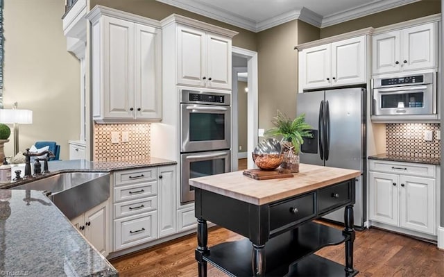 kitchen with a sink, white cabinetry, appliances with stainless steel finishes, crown molding, and dark wood-style flooring