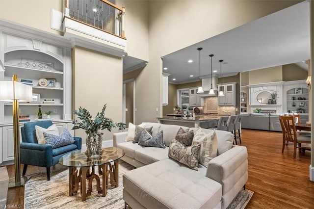 living area featuring recessed lighting, wood finished floors, a towering ceiling, and crown molding