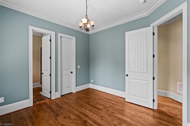 spare room featuring a chandelier, crown molding, baseboards, and wood finished floors