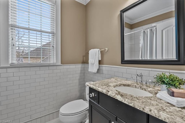 full bathroom featuring toilet, vanity, ornamental molding, wainscoting, and tile walls