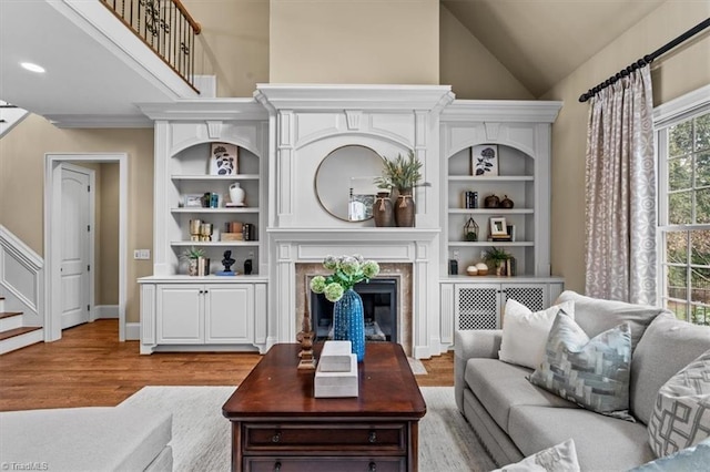 living area with built in features, stairway, wood finished floors, and a high end fireplace