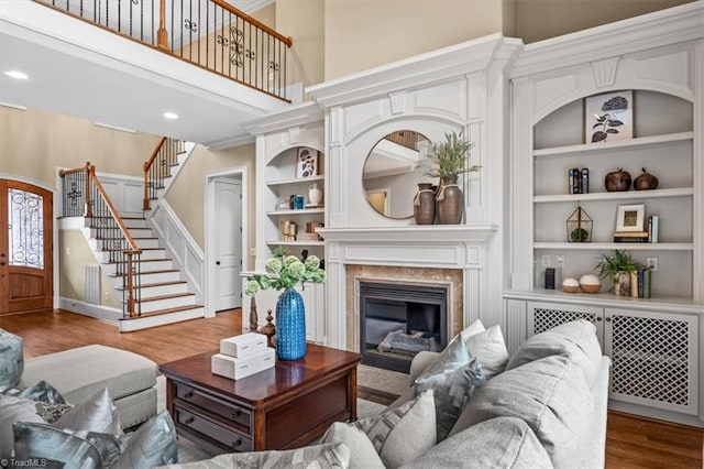 living room with built in features, wood finished floors, a high ceiling, a fireplace, and stairs