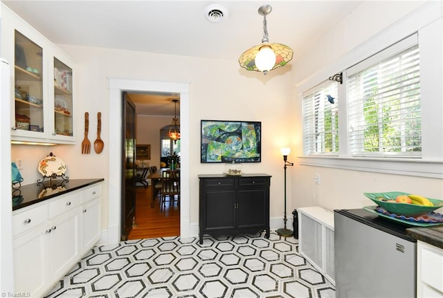 interior space featuring stainless steel fridge, decorative light fixtures, white cabinetry, and light hardwood / wood-style flooring