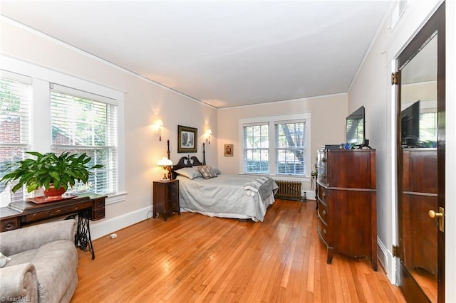 bedroom featuring radiator, ornamental molding, light hardwood / wood-style floors, and multiple windows