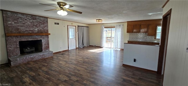 unfurnished living room featuring wooden walls, a fireplace, ornamental molding, ceiling fan, and dark wood-type flooring