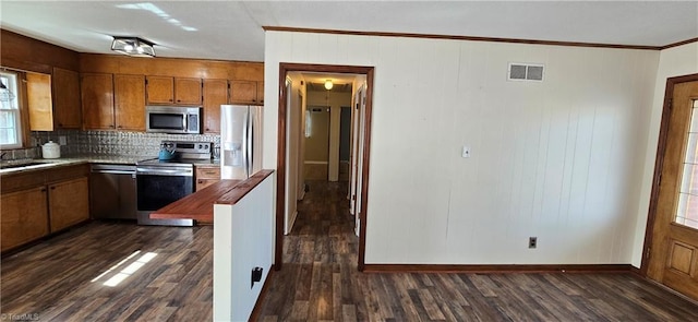 kitchen featuring sink, dark wood-type flooring, appliances with stainless steel finishes, backsplash, and ornamental molding