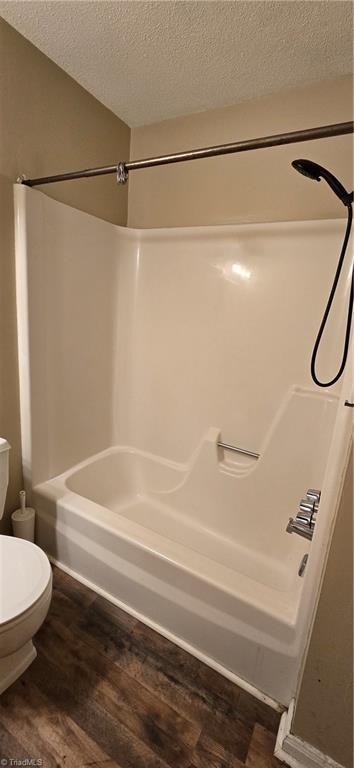 bathroom featuring hardwood / wood-style flooring, washtub / shower combination, toilet, and a textured ceiling