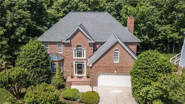 colonial inspired home with a chimney, driveway, a garage, and brick siding