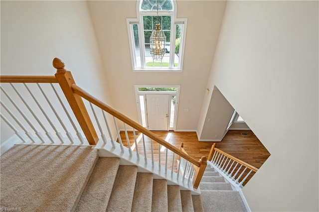 staircase with a high ceiling, a chandelier, wood finished floors, and baseboards