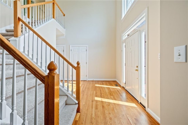 foyer featuring a towering ceiling, stairs, light wood-style flooring, and baseboards