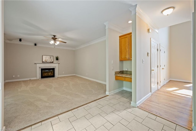 unfurnished living room with ceiling fan, crown molding, baseboards, light colored carpet, and a fireplace with flush hearth