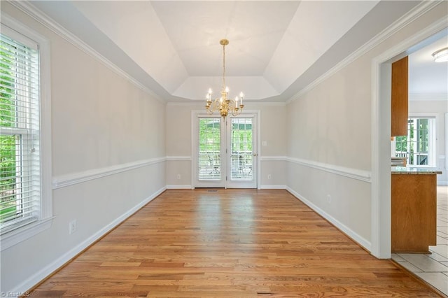 unfurnished dining area featuring a chandelier, healthy amount of natural light, light wood-style floors, a tray ceiling, and crown molding