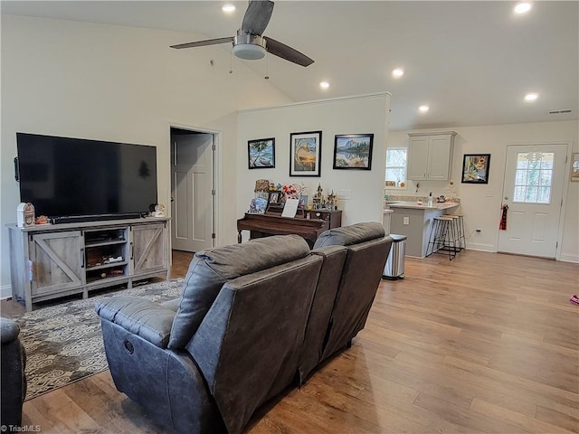 living room with ceiling fan, vaulted ceiling, and light wood-type flooring