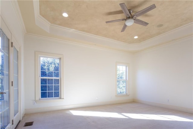 spare room with ornamental molding, a wealth of natural light, light colored carpet, and a tray ceiling