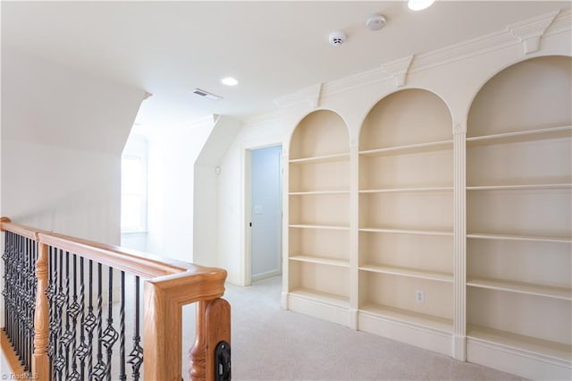 corridor featuring built in shelves, crown molding, and carpet