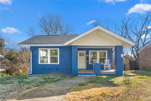 bungalow-style home with brick siding, roof with shingles, covered porch, a front yard, and crawl space