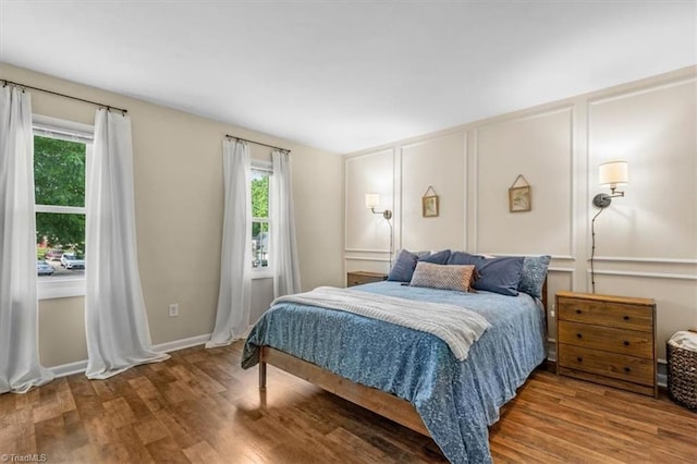 bedroom with multiple windows, wood finished floors, and a decorative wall
