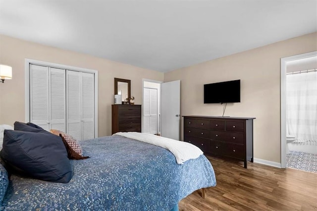 bedroom with baseboards, ensuite bathroom, a closet, and wood finished floors