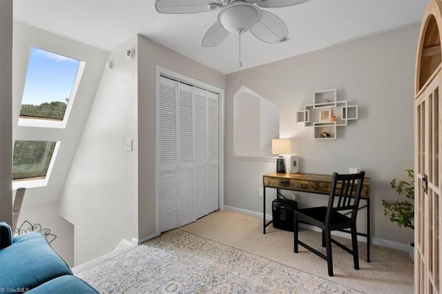 carpeted home office with baseboards, a ceiling fan, and a skylight